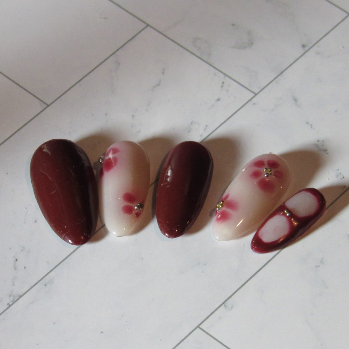 Set of four nail polish samples with floral designs on a tiled floor.