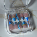 A set of 10 false press-on nails displayed in a clear plastic case on a white marble surface. The nails feature a mix of solid light pink, bright blue, black-and-white zebra stripes, leopard print, and gold glitter accents.