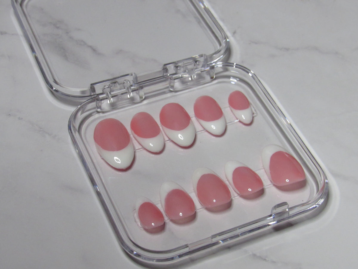 A set of ten press-on nails with a pink and white French tip design, displayed inside a clear plastic case on a light marble surface.