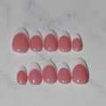 Ten false press-on nails arranged in two rows on a white marble surface, featuring a classic French tip design with a glossy pink base and a white tip.
